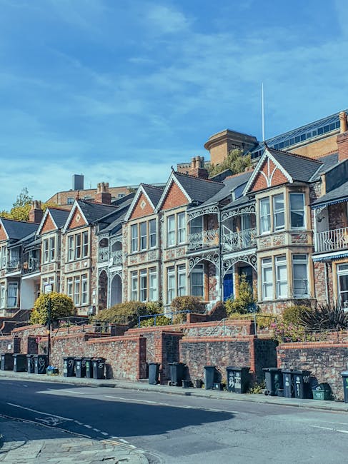 A narrow cobblestone street in West Hampstead, bordered by historic brick residential buildings on both sides. On the left, part of a dark brick wall and a black metal railing are visible, with a classic white lamp post attached to the building. The building features a bay window with white trim and a small awning. Further along, a white bay window structure can be seen on the near-facing building, which has a textured brick finish. The street curves gently to the right, leading toward a small brick wall and gate in the background, with a leafless tree visible behind the wall. The lighting suggests a bright, clear day with natural sunlight casting subtle shadows along the pavement and buildings, creating a quiet, typical West Hampstead residential scene that could be part of an independent or private waste collection zone, reflecting the area’s characteristic mix of traditional architecture and modern urban infrastructure. As part of rubbish removal services, this setting highlights the importance of on-site clearance options in densely built neighbourhoods to maintain tidy and accessible street environments.